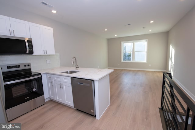 kitchen featuring sink, stainless steel appliances, light stone countertops, white cabinets, and kitchen peninsula