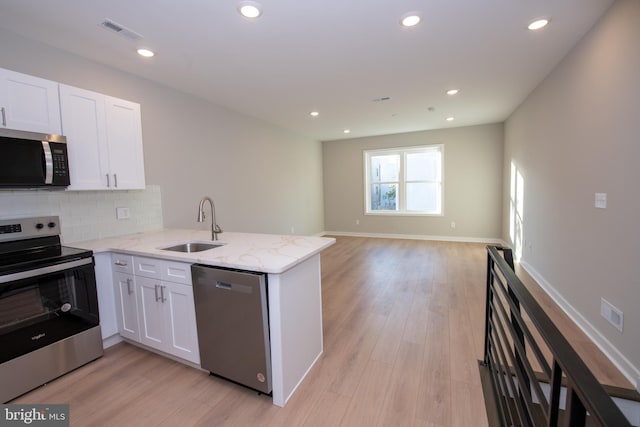 kitchen with sink, white cabinetry, appliances with stainless steel finishes, kitchen peninsula, and light stone countertops