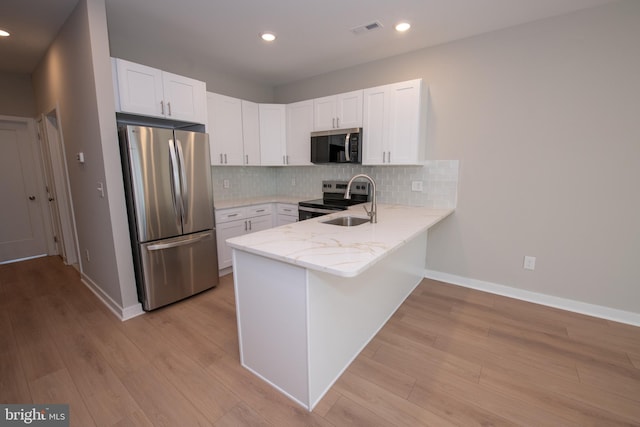 kitchen with sink, white cabinetry, light wood-type flooring, appliances with stainless steel finishes, and backsplash