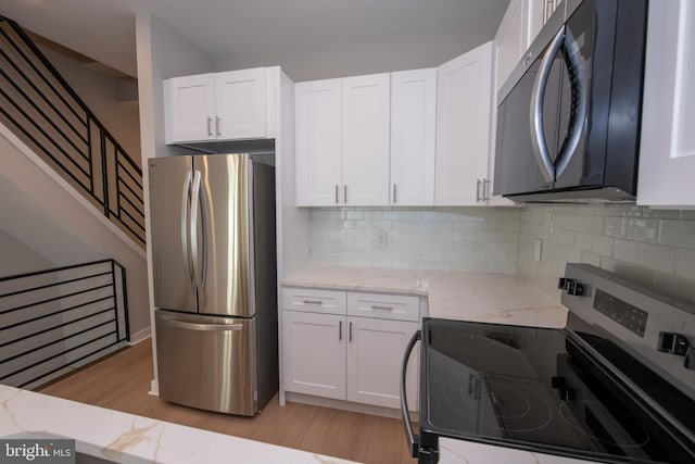 kitchen featuring white cabinetry, stainless steel appliances, light stone countertops, and decorative backsplash