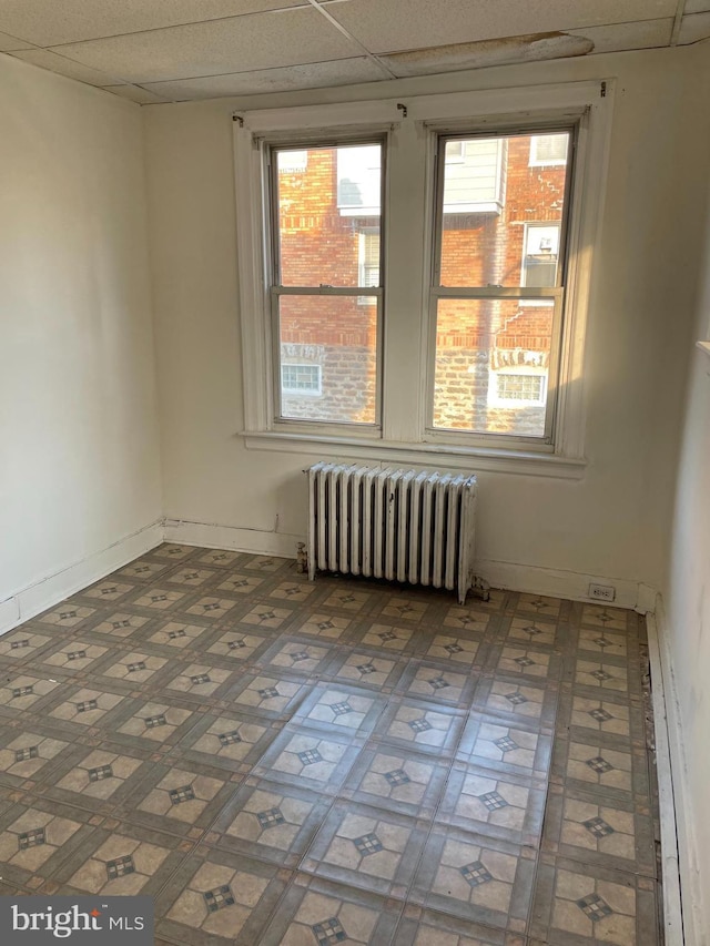 unfurnished room with radiator and a drop ceiling