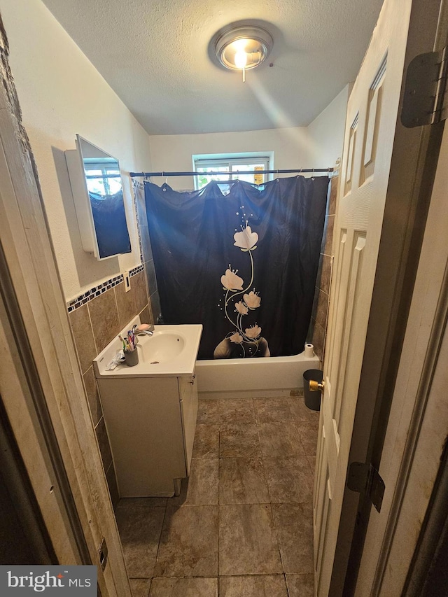 bathroom featuring shower / bath combination with curtain, vanity, a textured ceiling, and tile walls