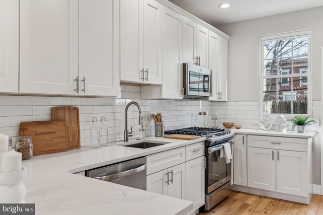 kitchen with backsplash, sink, stainless steel appliances, white cabinets, and light stone counters