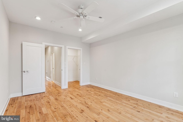 unfurnished bedroom featuring light wood-type flooring, ceiling fan, a walk in closet, and a closet