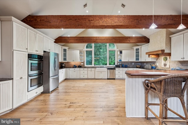 kitchen with kitchen peninsula, a kitchen breakfast bar, stainless steel appliances, decorative light fixtures, and white cabinets