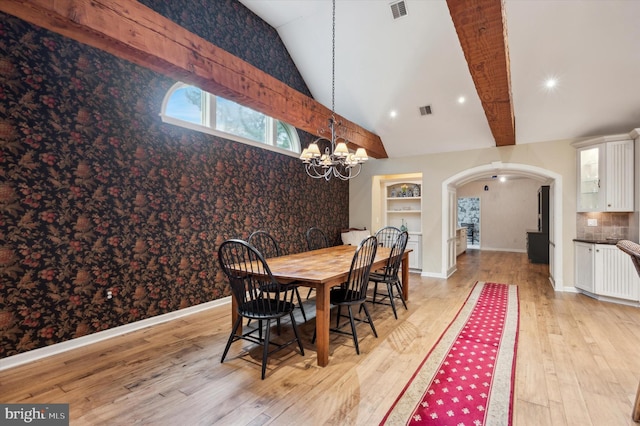 dining space featuring lofted ceiling with beams, light hardwood / wood-style flooring, and a chandelier