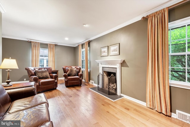 living room with a high end fireplace, a healthy amount of sunlight, light wood-type flooring, and crown molding