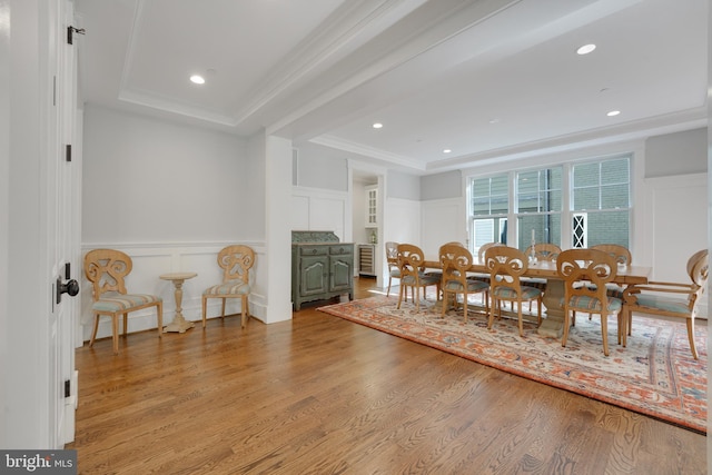 dining area with light wood-type flooring, crown molding, and a tray ceiling