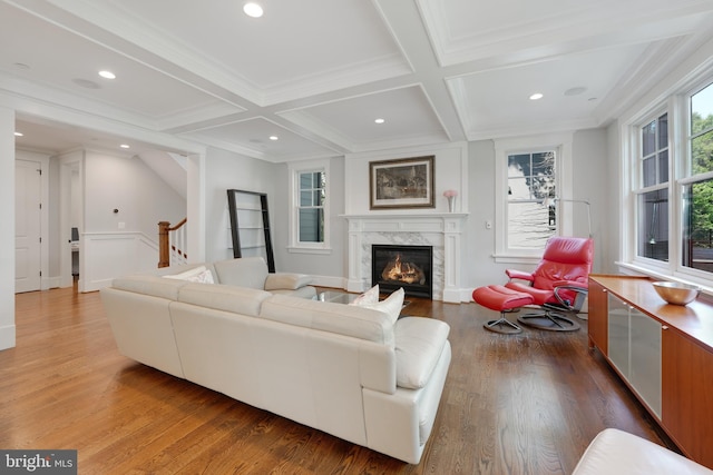 living room featuring coffered ceiling, beamed ceiling, wood-type flooring, a fireplace, and ornamental molding