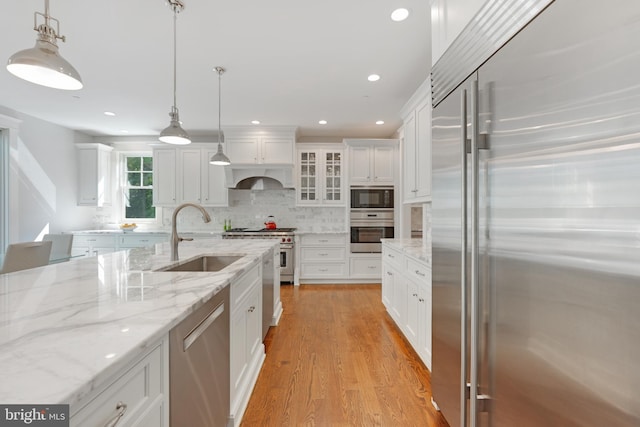 kitchen with light stone countertops, sink, built in appliances, white cabinets, and hanging light fixtures