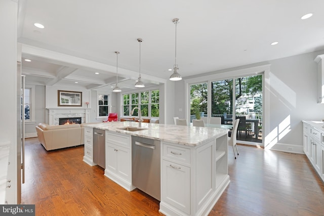 kitchen with beam ceiling, white cabinetry, sink, stainless steel dishwasher, and an island with sink