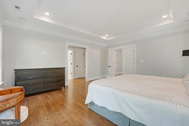 bedroom featuring a raised ceiling, ornamental molding, and light hardwood / wood-style flooring