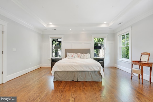 bedroom with light wood-type flooring, a raised ceiling, and crown molding