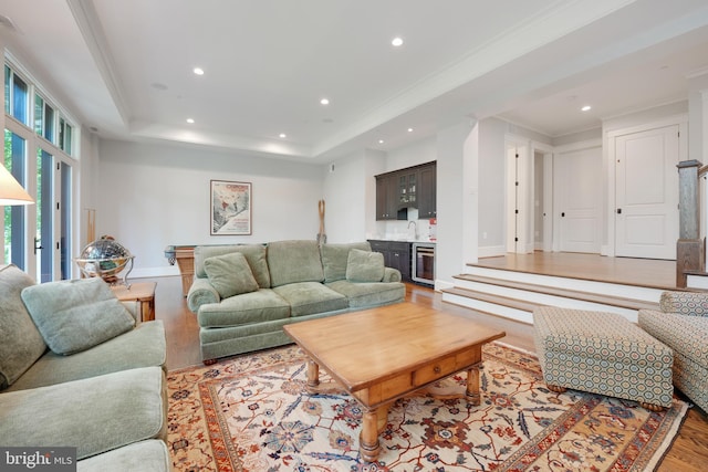 living room featuring a tray ceiling, crown molding, wet bar, light hardwood / wood-style flooring, and wine cooler