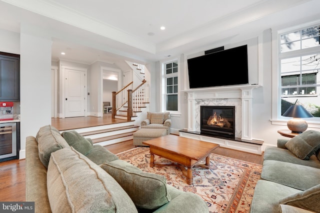 living room featuring light hardwood / wood-style flooring, ornamental molding, a fireplace, a tray ceiling, and beverage cooler