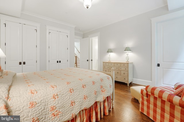 bedroom with ornamental molding, multiple closets, and dark wood-type flooring