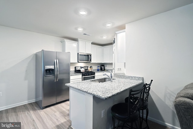 kitchen with white cabinetry, sink, stainless steel appliances, a kitchen breakfast bar, and kitchen peninsula