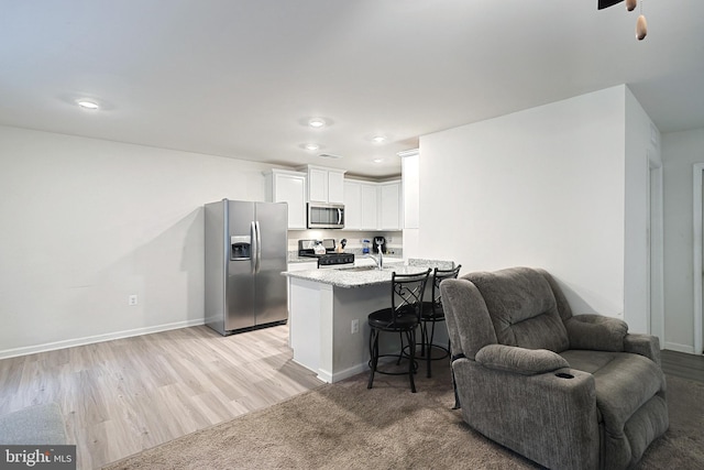 kitchen featuring light stone countertops, appliances with stainless steel finishes, a kitchen breakfast bar, light hardwood / wood-style flooring, and white cabinets