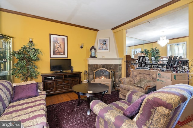 living room featuring hardwood / wood-style floors, a stone fireplace, ornamental molding, and a chandelier