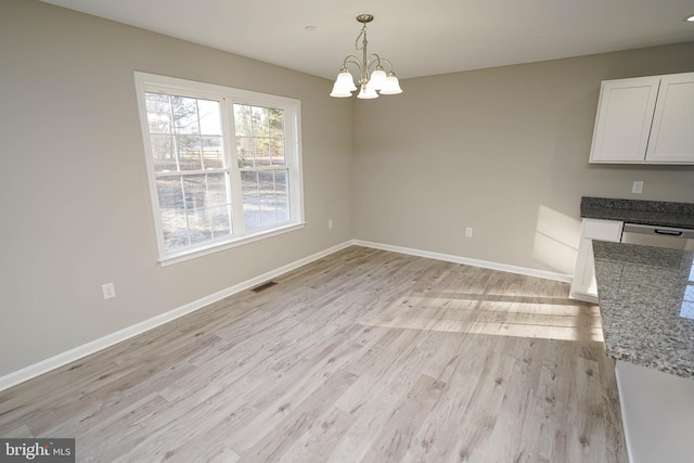 unfurnished dining area featuring light wood-type flooring and an inviting chandelier