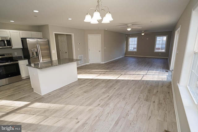 kitchen with dark stone counters, hanging light fixtures, stainless steel appliances, and light hardwood / wood-style floors