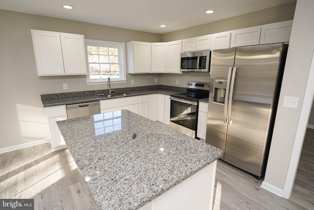 kitchen with a center island, sink, light stone countertops, appliances with stainless steel finishes, and white cabinetry