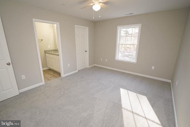 unfurnished bedroom featuring a closet, light colored carpet, ensuite bath, and ceiling fan