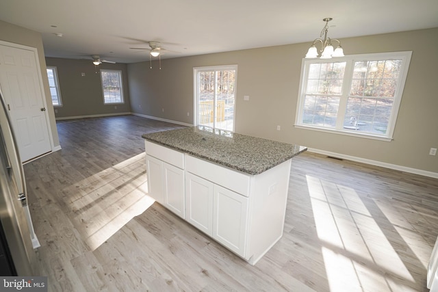 kitchen featuring white cabinetry, hanging light fixtures, dark stone counters, ceiling fan with notable chandelier, and light wood-type flooring