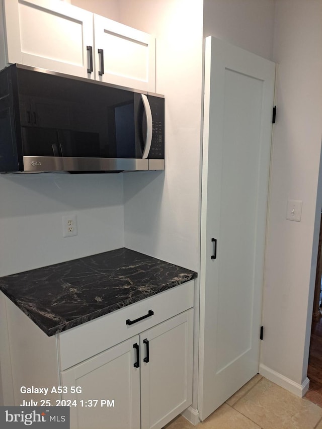 kitchen featuring white cabinetry, light tile patterned floors, and dark stone counters