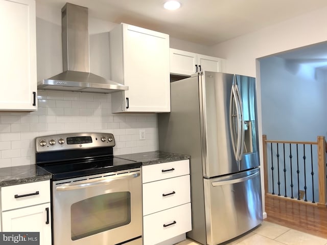 kitchen featuring white cabinetry, dark stone countertops, light tile patterned floors, stainless steel appliances, and wall chimney range hood