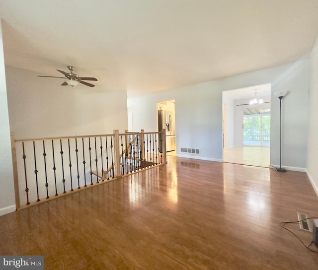 spare room featuring wood-type flooring and ceiling fan with notable chandelier