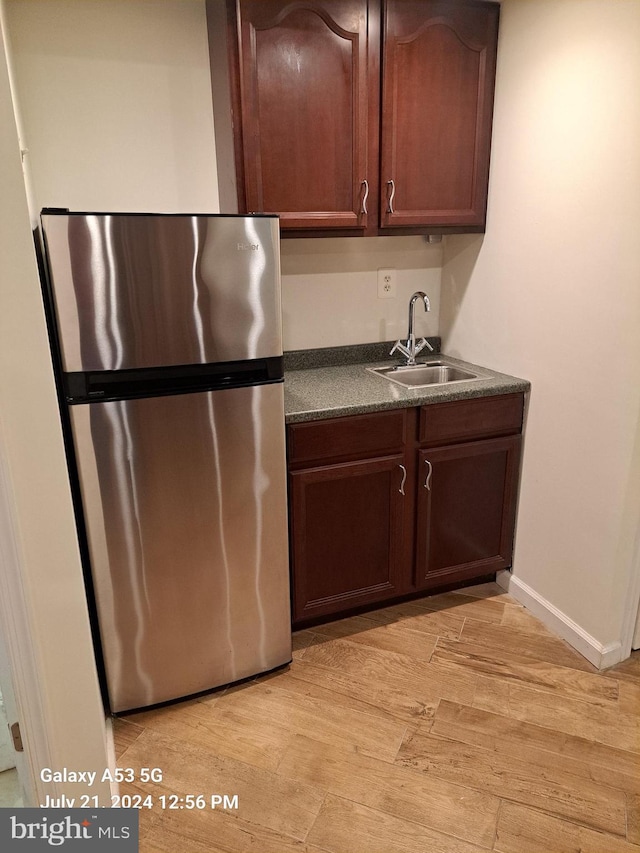 kitchen featuring sink, dark brown cabinets, light hardwood / wood-style flooring, and stainless steel refrigerator