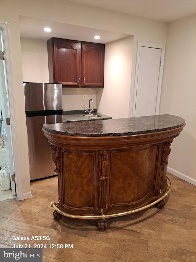 bar featuring dark brown cabinetry, sink, stainless steel refrigerator, and light hardwood / wood-style flooring