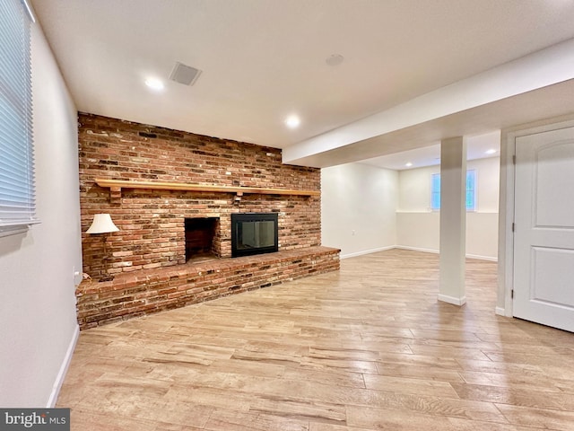 unfurnished living room featuring brick wall, a fireplace, and light hardwood / wood-style flooring