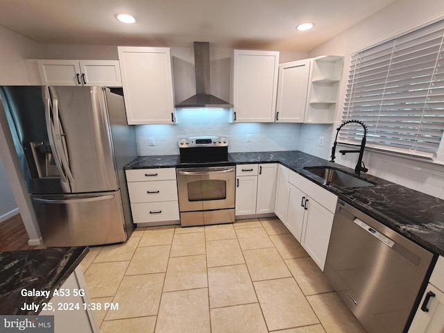 kitchen featuring sink, white cabinetry, dark stone countertops, appliances with stainless steel finishes, and wall chimney range hood