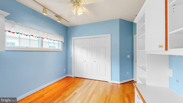 unfurnished bedroom with light wood-type flooring, a closet, track lighting, and ceiling fan