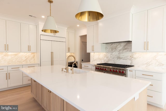 kitchen with decorative backsplash, premium appliances, a large island with sink, decorative light fixtures, and white cabinets