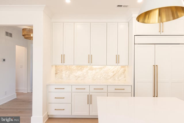 kitchen with paneled refrigerator, tasteful backsplash, crown molding, white cabinets, and light wood-type flooring