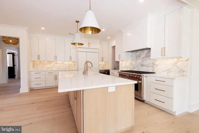 kitchen with high quality appliances, a center island with sink, white cabinets, and decorative light fixtures