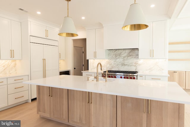 kitchen with a center island with sink, white cabinetry, hanging light fixtures, and sink