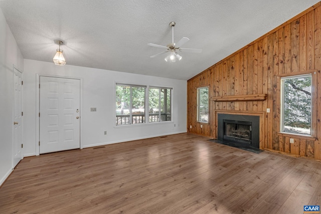 unfurnished living room featuring a textured ceiling, vaulted ceiling, ceiling fan, hardwood / wood-style floors, and wood walls