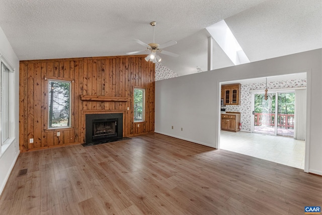 unfurnished living room with wood walls, lofted ceiling, light hardwood / wood-style flooring, ceiling fan, and a large fireplace