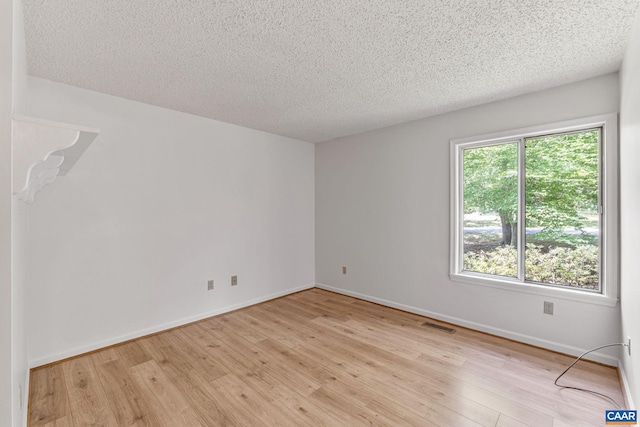 spare room with a textured ceiling and light hardwood / wood-style floors