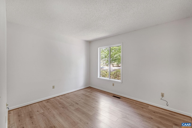 empty room with a textured ceiling and light hardwood / wood-style flooring