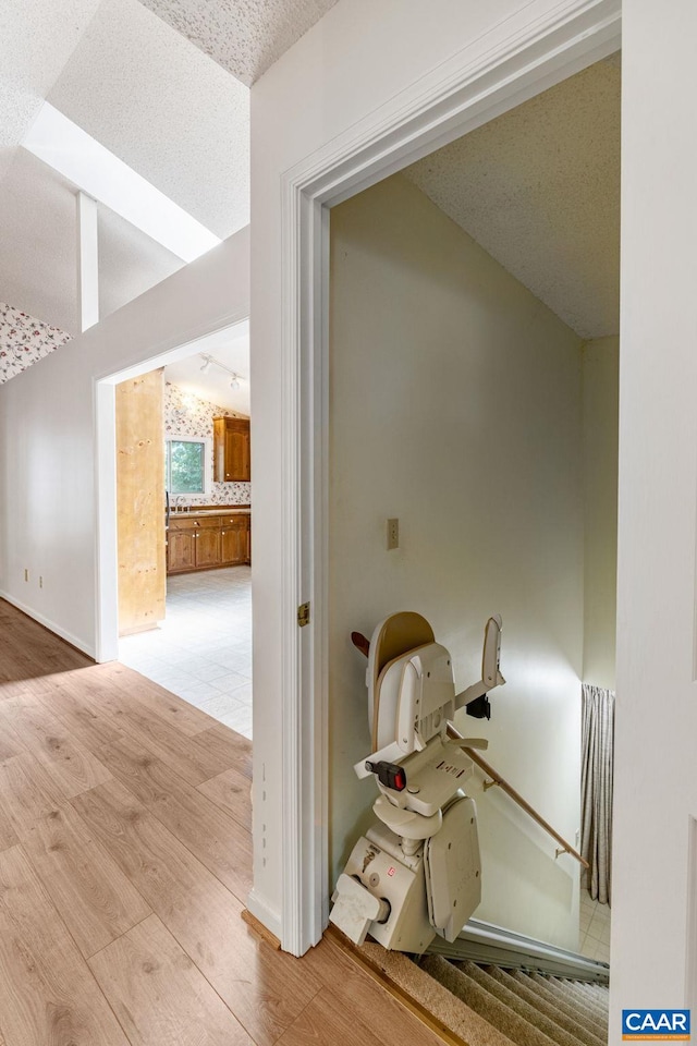 hallway featuring a textured ceiling, light hardwood / wood-style flooring, and lofted ceiling