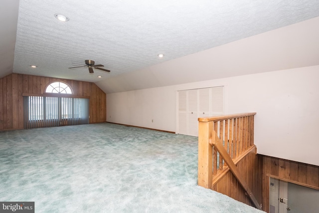 bonus room with wooden walls, a textured ceiling, ceiling fan, and vaulted ceiling