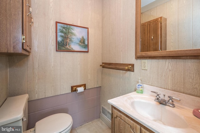 bathroom with wood walls, tile patterned floors, toilet, and vanity