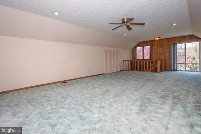 carpeted empty room with ceiling fan, a textured ceiling, wood walls, and vaulted ceiling