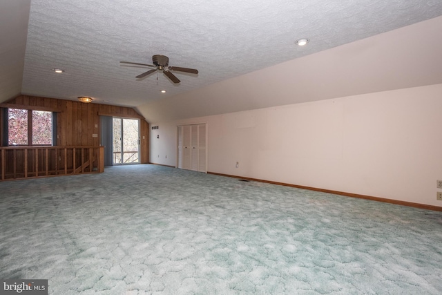 interior space with ceiling fan, vaulted ceiling, wood walls, carpet, and a textured ceiling