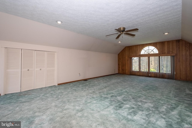 additional living space with wood walls, carpet flooring, a textured ceiling, and vaulted ceiling